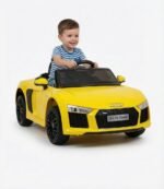 Enfant portant un casque et des lunettes de soleil assis au volant d'une voiture électrique enfant Audi R8 Spyder 12V jaune avec logo quatre anneaux et plaque DLX R8 Spyder