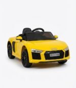 Enfant portant un casque et des lunettes de soleil assis au volant d'une voiture électrique enfant Audi R8 Spyder 12V jaune avec logo quatre anneaux et plaque DLX R8 Spyder